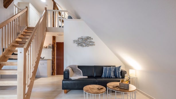 Ein moderner Wohnbereich im Loft-Stil mit Treppe, einem schwarzen Ledersofa, zwei runden Tischen und einem Wandbild mit einem Fischmotiv.