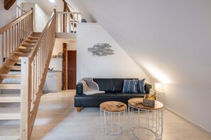 Un espace de vie moderne de style loft, comprenant un escalier, un canapé en cuir noir, deux tables rondes et une œuvre d'art représentant des poissons, accrochée au mur.