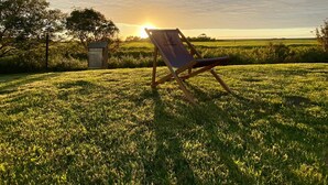 A grassy field with a wooden chair and a small shed. - Knutzenswarft - Holiday Apartment "Möwe" (Westerhever)