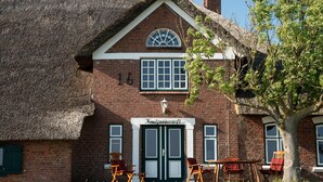 A brick building with a thatched roof, a double door entrance, and a sign reading 'Kunsthaus'. - Knutzenswarft - Holiday Apartment "Möwe" (Westerhever)