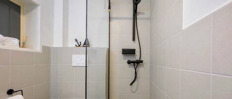 A bathroom with a toilet, a shower with a handheld showerhead, and a towel rack.