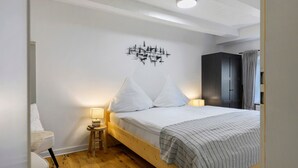 A bedroom with a wooden bed, white walls, a small bedside table with a lamp, and a dark wardrobe. - Knutzenswarft - Holiday Apartment "Möwe" (Westerhever)