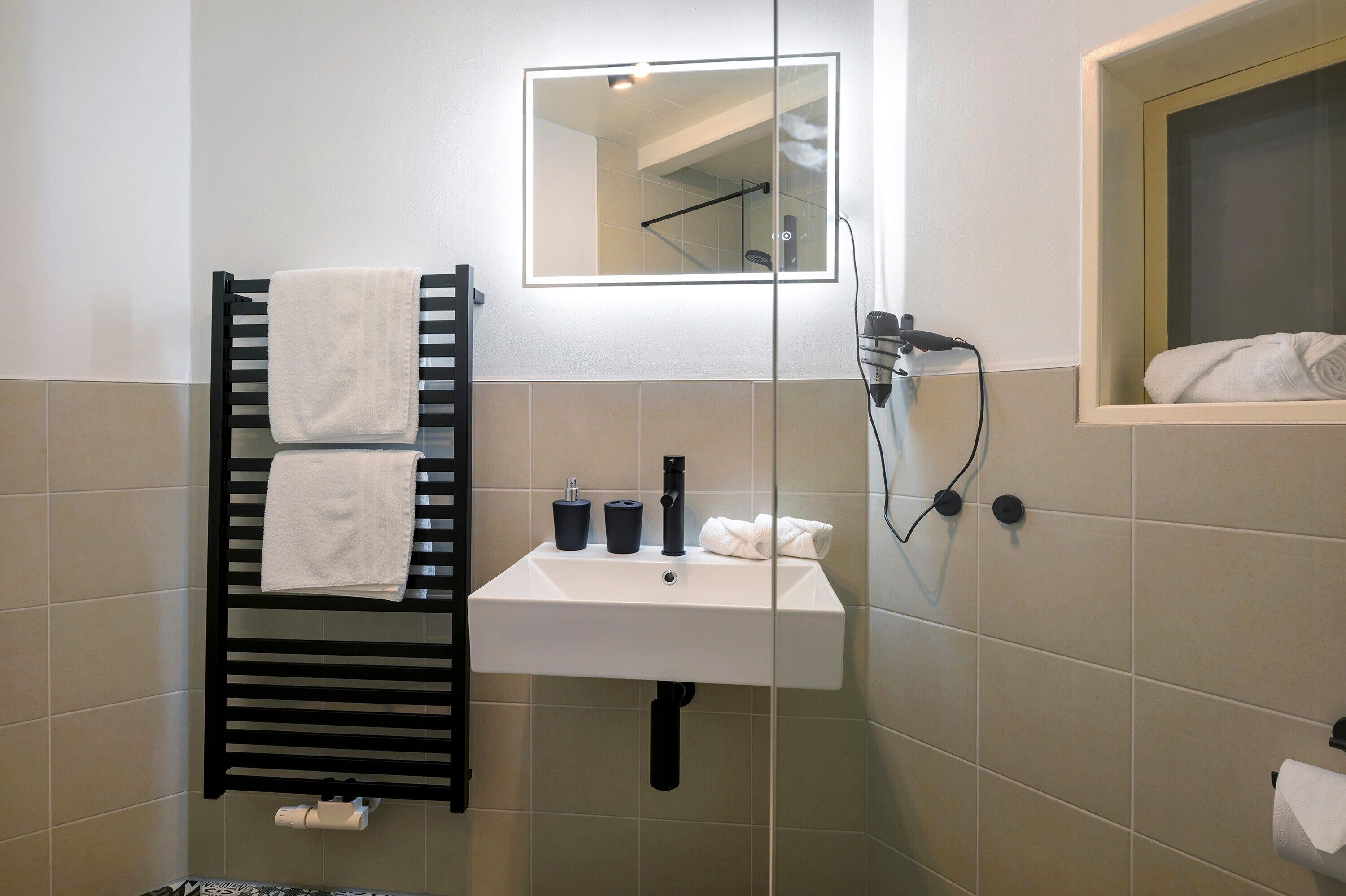 A bathroom with a black towel rack, a white sink, a mirror, and a shower area.