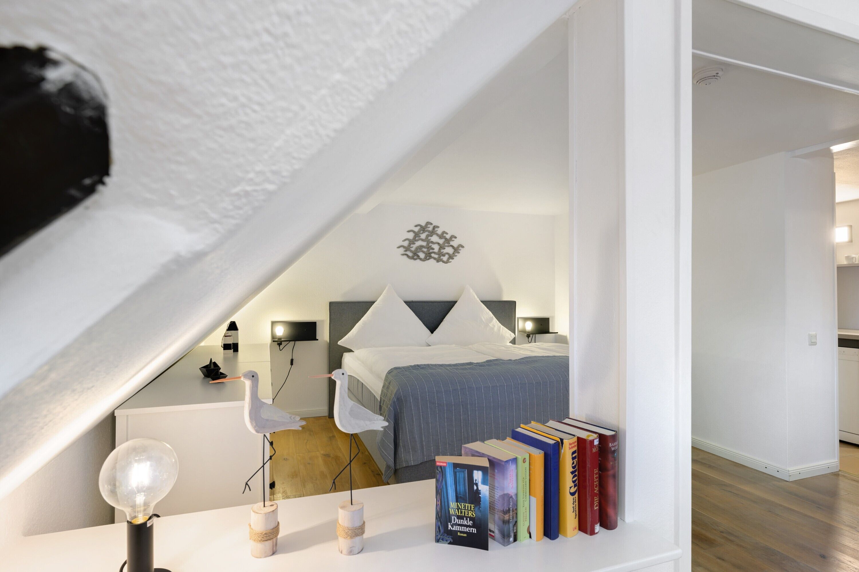 Une chambre à coucher avec un lit, une bibliothèque remplie de livres, une lampe et un oiseau décoratif.
