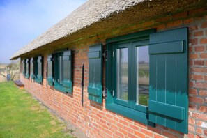 Un edificio de ladrillo con contraventanas verdes y techo de paja.