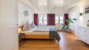 A bedroom with a bed, a nightstand, a dresser, a window, and a potted plant. - Knutzenswarft - Holiday Apartment "Strandläufer" (Westerhever)