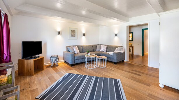 A modern living room with a sofa, a TV on a wooden stand, two side tables, and a patterned rug. - Knutzenswarft - Holiday Apartment "Strandläufer" (Westerhever)