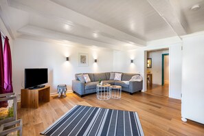 A modern living room with a sofa, a TV on a wooden stand, two side tables, and a patterned rug.