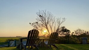 Two Adirondack chairs facing a sunset over a grassy field with a wooden fence and a small structure in the background. - Knutzenswarft - Holiday Apartment "Strandläufer" (Westerhever)