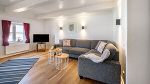 A modern living room with a grey sofa, a flat-screen TV, a wooden coffee table, and a striped rug. - Knutzenswarft - Holiday Apartment "Strandläufer" (Westerhever)