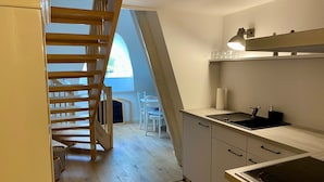 Une cuisine équipée d’une cuisinière, d’un évier et d’un escalier en bois menant à un coin repas.