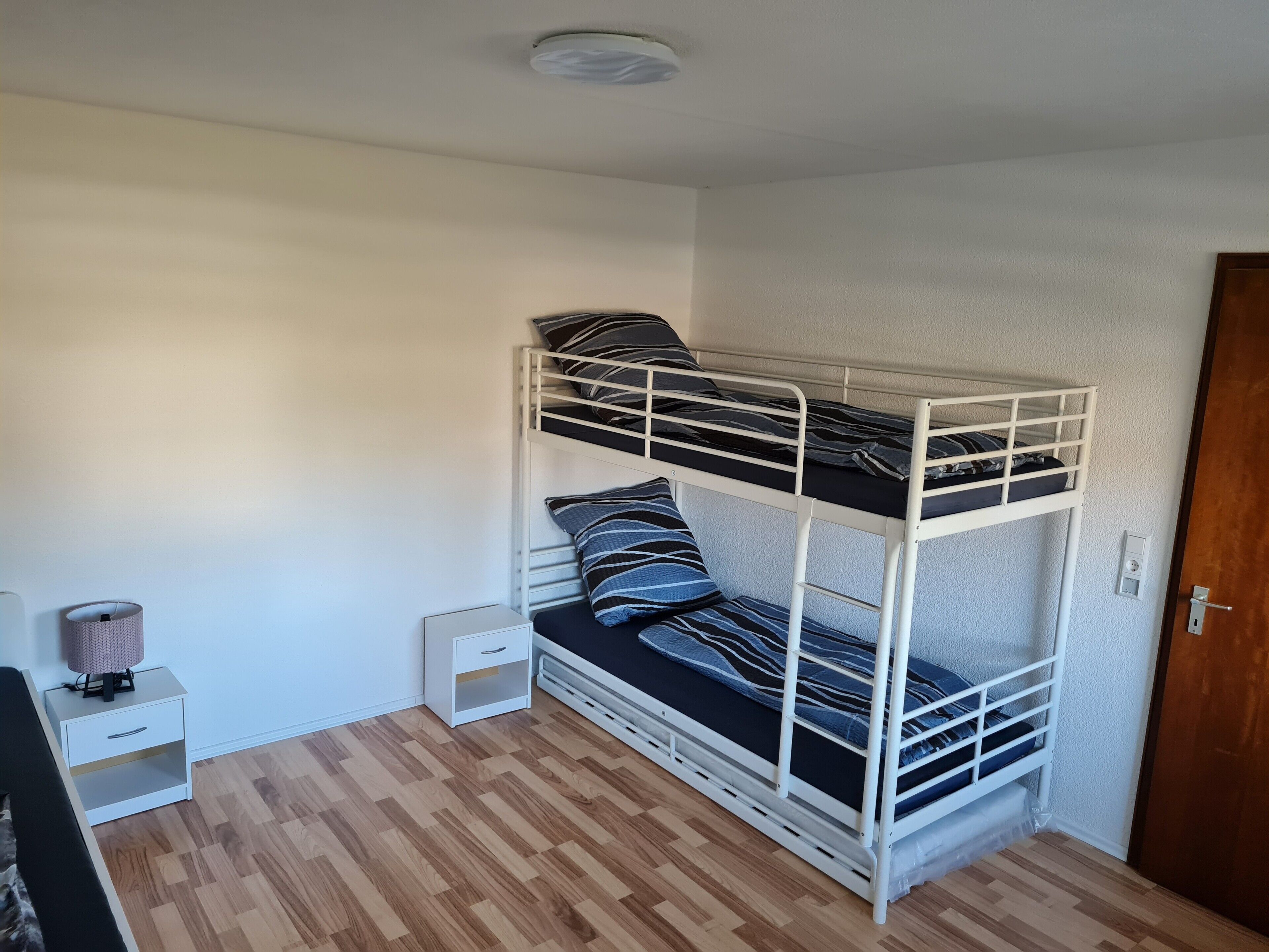 Ein Etagenbett mit zwei Schlafstellen, ein kleiner Nachttisch, eine Lampe und ein Holzboden.