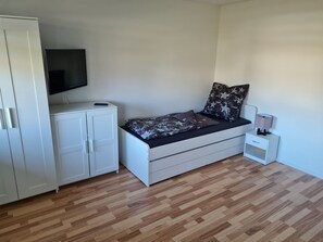 A bedroom with a bed, a TV mounted on a cabinet, a bedside table with a lamp, and a wardrobe.