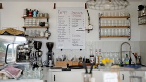 Interior de una cafetería con un menú, máquinas de espresso, estanterías con tazas y un letrero colgante.