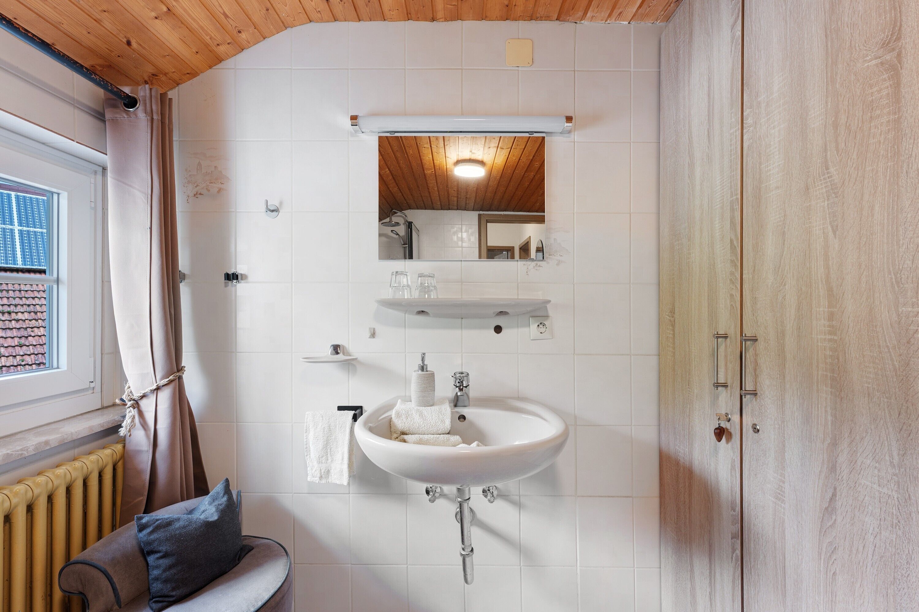 A bathroom with a white sink, a mirror, a towel rack, and a wooden ceiling.