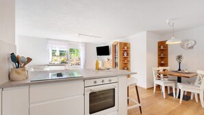 A kitchen with a central island, wooden shelves, a dining table with chairs, and a clock on the wall. - Holiday Apartment 'Vergissmeinnicht' with Mountain View, Shared Garden and Wi-Fi (Kirchzarten)