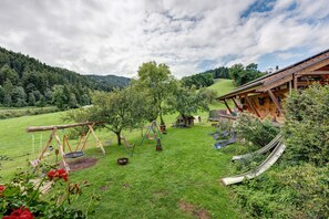 A rustic wooden cabin with a swing set and slide in a lush green field.