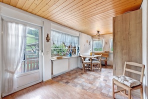 A room with a wooden ceiling, a dining table with chairs, a window with curtains, and a radiator.