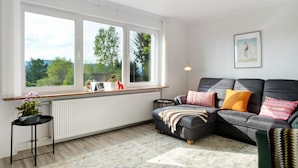 Un salon avec un canapé, une fenêtre donnant sur un beau paysage, un radiateur et une petite table sur laquelle est posée une plante.