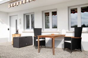 An outdoor patio with a table and two chairs, a speaker, and a small wooden stool.