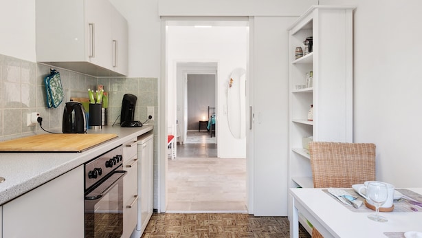 Une cuisine avec des armoires blanches, un plan de travail en bois et un coin repas avec une table mise pour deux personnes.