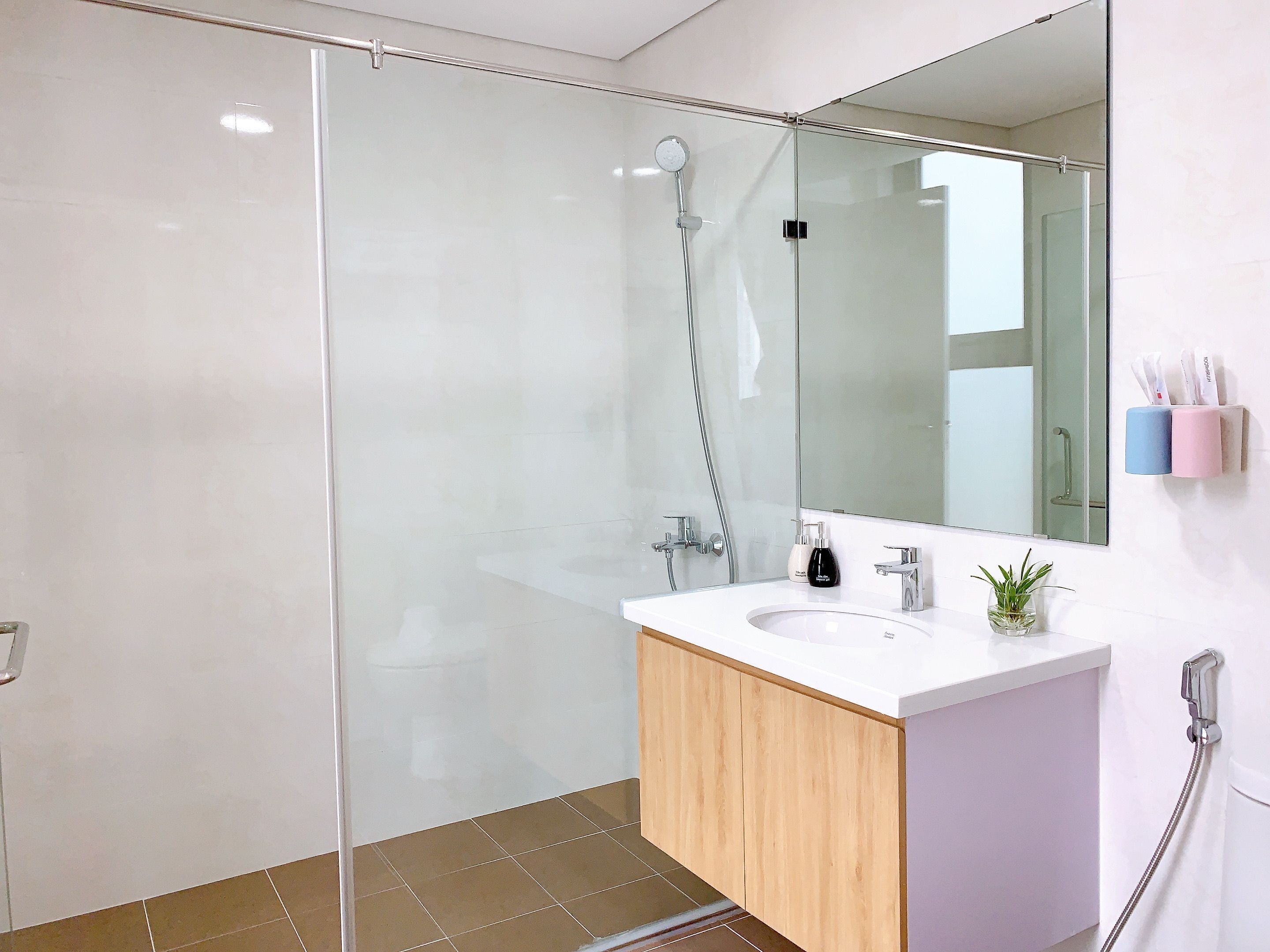 A modern bathroom with a glass shower enclosure, a white sink, and a wooden vanity.