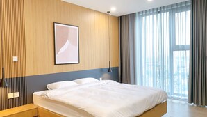 A modern bedroom with a large bed, wooden panel walls, a city view, and a pendant light. - Ha Tay Millennium Apartments - Free Gym Pool (Hanoi)