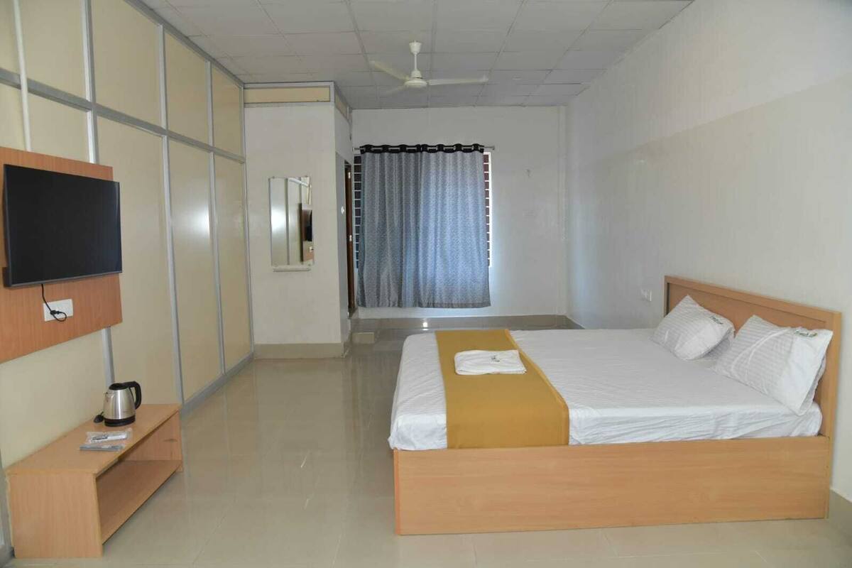 A hotel room with a bed, a TV, a coffee maker, and a window with curtains.
