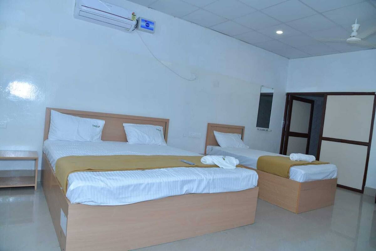 A hotel room with two beds, a wooden headboard, a bedside table, an air conditioning unit, and a door with a mirror.