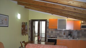 A cozy living room with a sofa and a dining table, a kitchen with orange cabinets and a microwave, and a wooden ceiling.