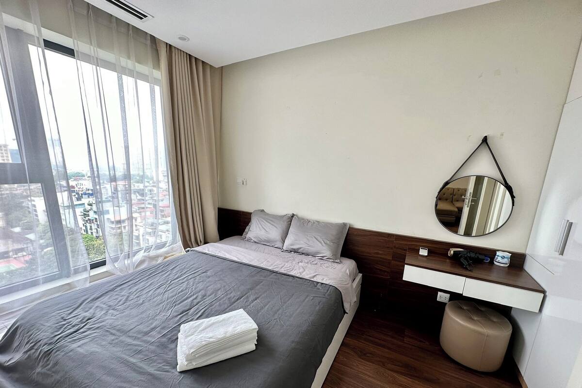 Une chambre d’hôtel avec un grand lit, une table de chevet avec un miroir et une vue sur la ville par la fenêtre.