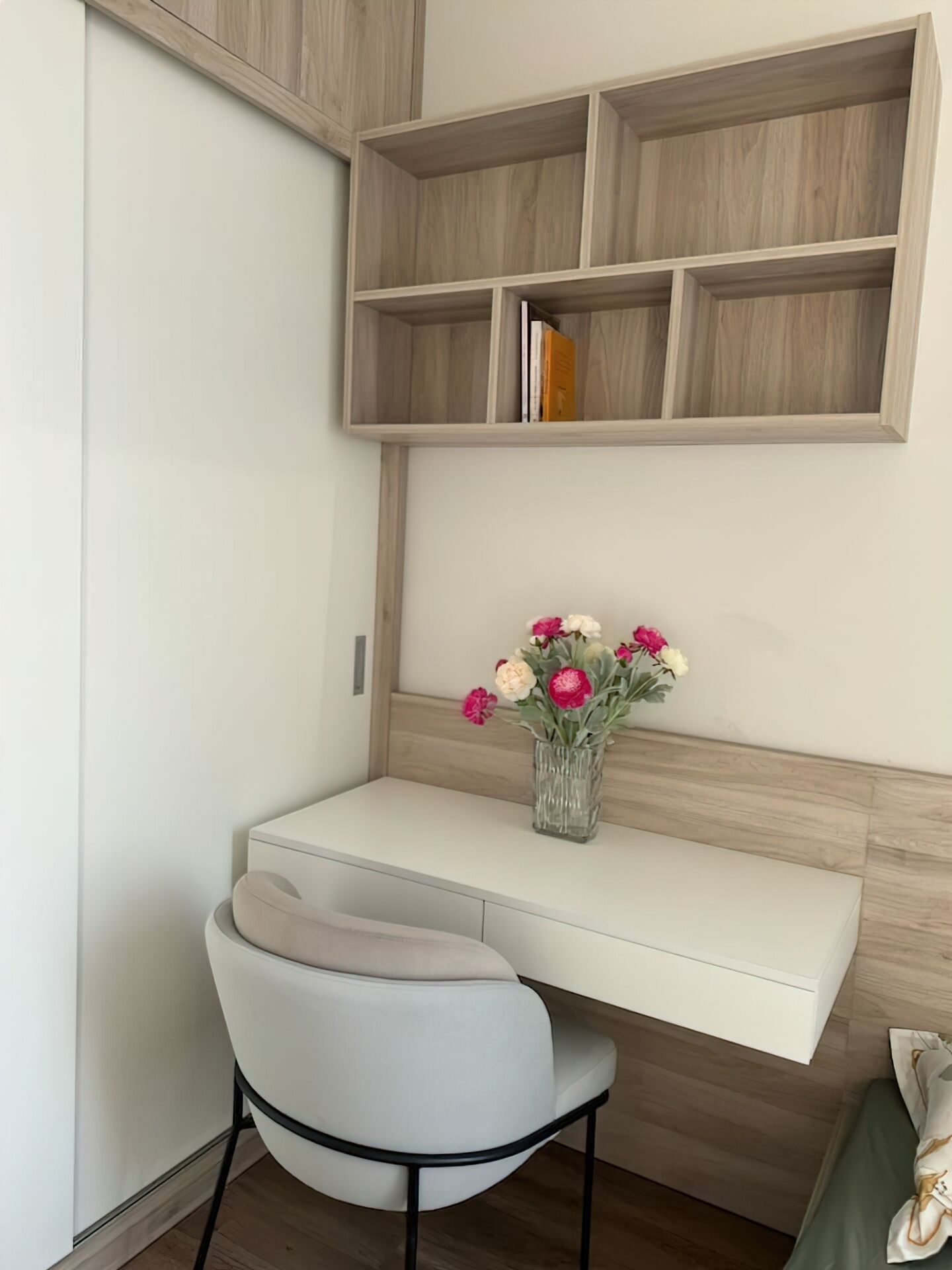 Una scrivania d'angolo con una sedia, un vaso di fiori e mensole in legno sopra.