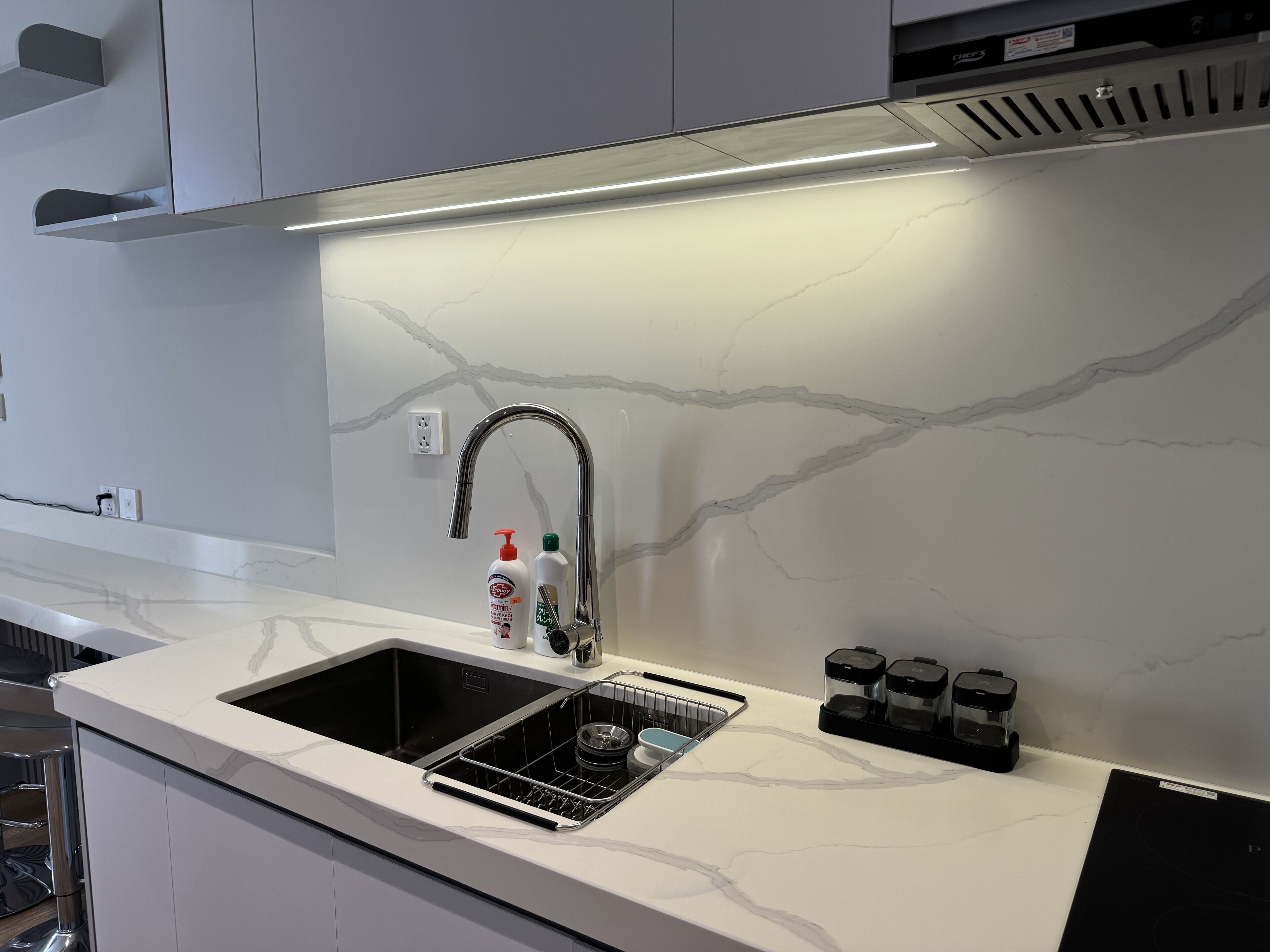 A modern kitchen with a white marble backsplash, stainless steel sink, and black appliances.