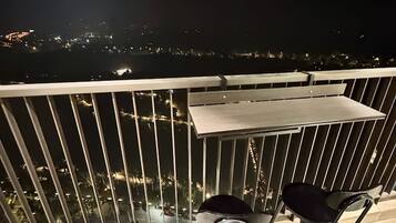 A balcony with a table and two chairs, overlooking a cityscape at night.