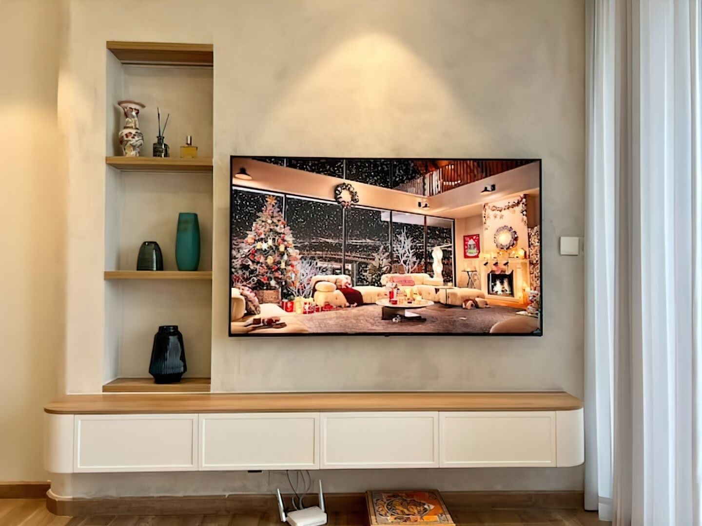 Ein Wohnzimmer mit einem großen Flachbildfernseher an der Wand, einer Holzlounge darunter und einem Weihnachtsbaum links.
