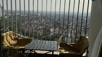 A balcony with a table and two chairs, overlooking a cityscape.