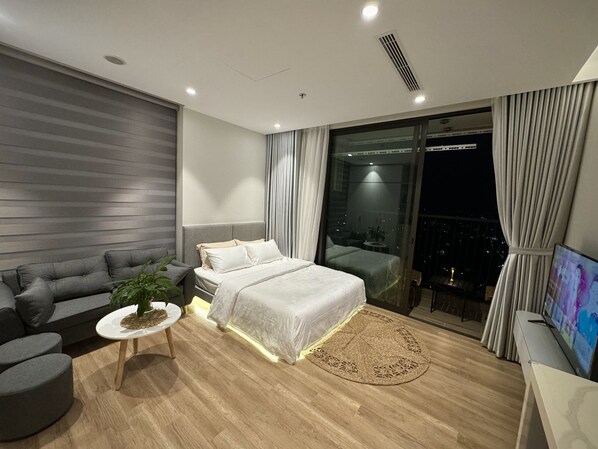 A modern bedroom with a large bed, a sofa, a small table, and a TV.