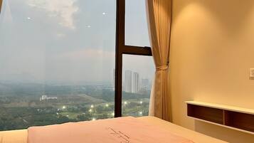 Ein Schlafzimmer mit großem Fenster, einem Bett mit rosa Bettdecke und Blick auf eine Stadtlandschaft.