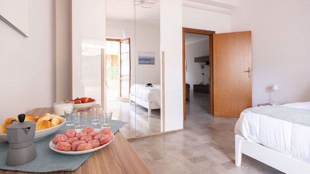 Une chambre d’hôtel avec un lit, une table de petit-déjeuner avec des viennoiseries et du café, et une vue sur le balcon.