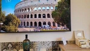 A television displaying a 4K image of the Colosseum with a bottle of Paris wine and a jar of Home Sweet Home sweetener on a table.