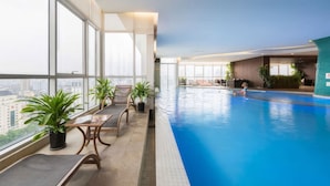 Une piscine intérieure avec vue sur la ville, un coin salon agrémenté de plantes et un enfant qui joue dans l’eau.