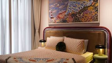 A bedroom with a bed, a painting, a hanging light fixture, and a nightstand.