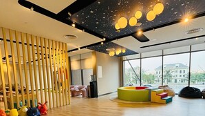 Une pièce spacieuse avec un plancher en bois, un espace de jeux avec des jouets colorés et un plafond décoré de motifs étoilés.