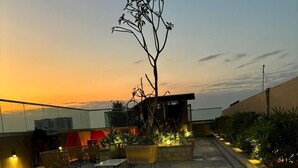Une terrasse sur le toit, avec un espace salon, un petit arbre et une vue sur le coucher du soleil.