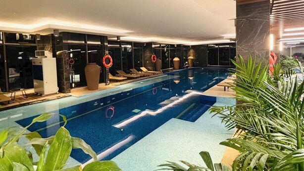 Une piscine intérieure à l’eau claire, entourée de chaises longues et de plantes en pot.