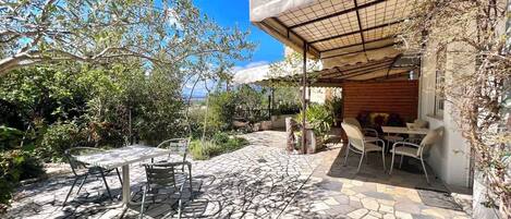 An outdoor patio with stone flooring, a table and chairs, and a pergola providing shade.