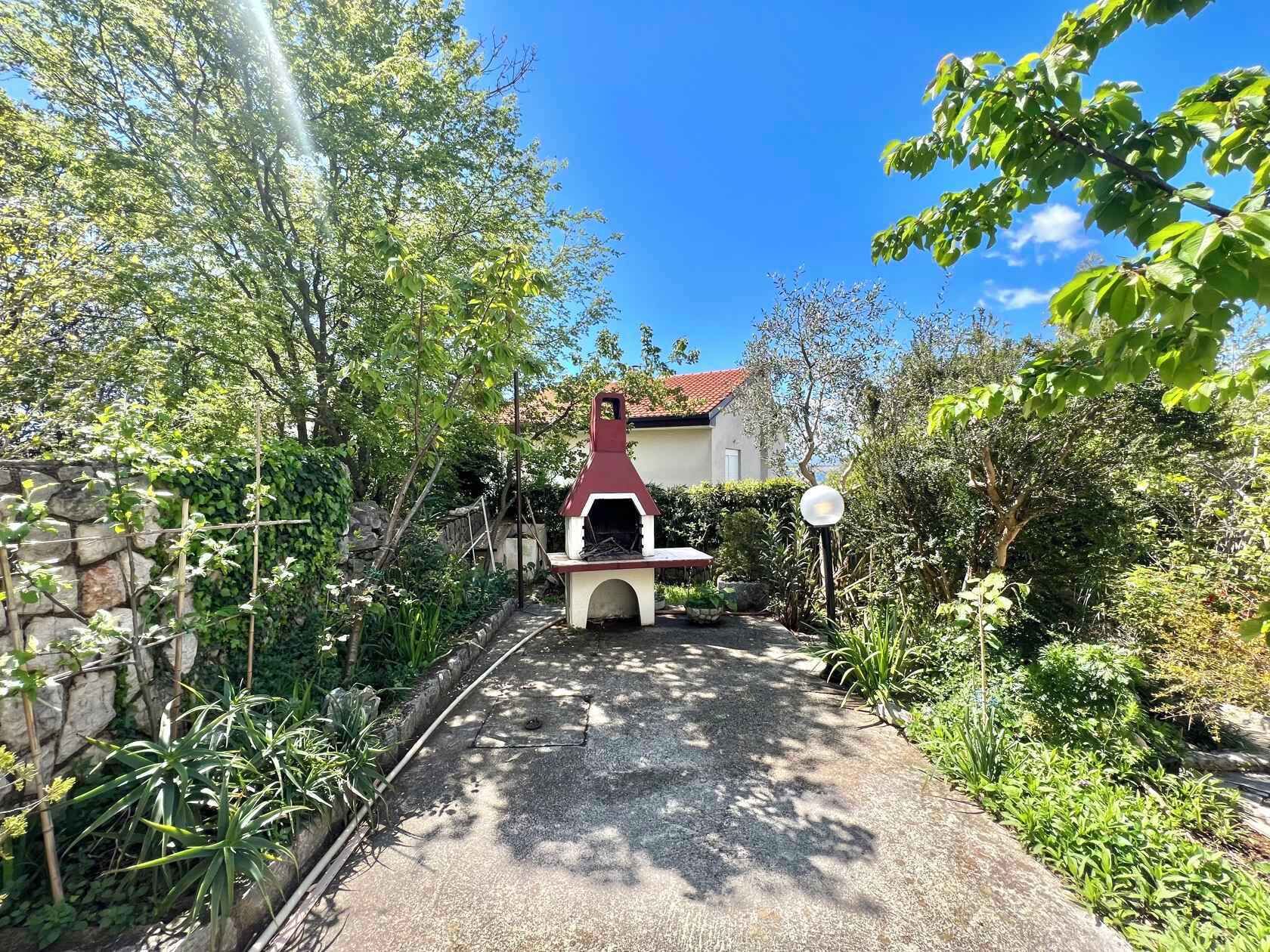 A pathway leading to a house with a red-roofed barbecue area surrounded by greenery.