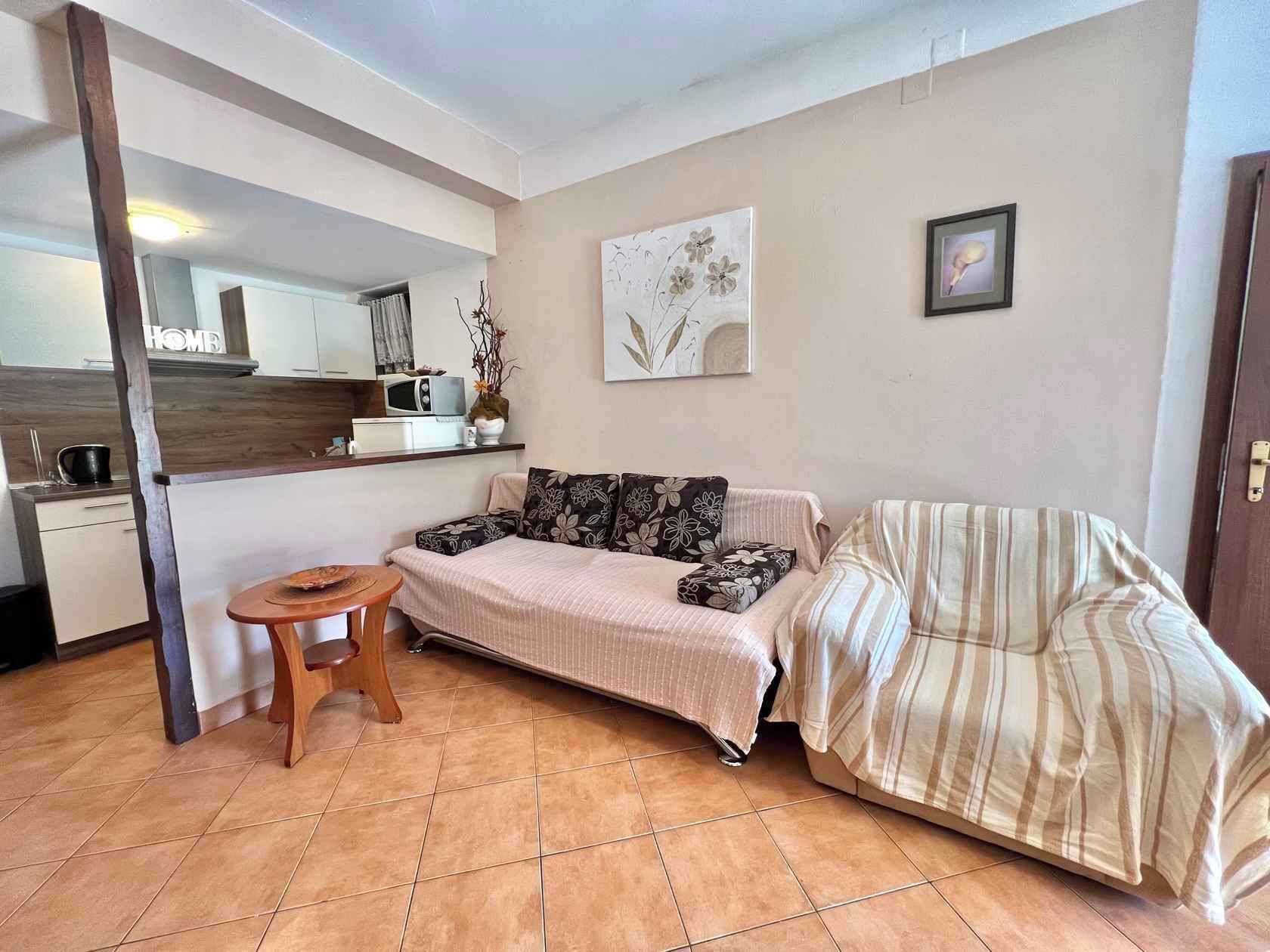 A compact living space with a sofa, a small table, a microwave, and a kitchen area.