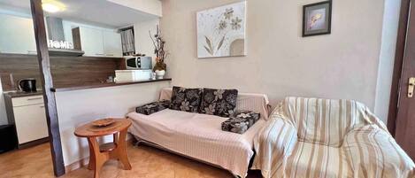 A compact living space with a sofa, a small table, a microwave, and a kitchen area.