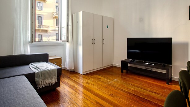 A modern living room with a sofa, a TV on a stand, wooden flooring, and a wardrobe.